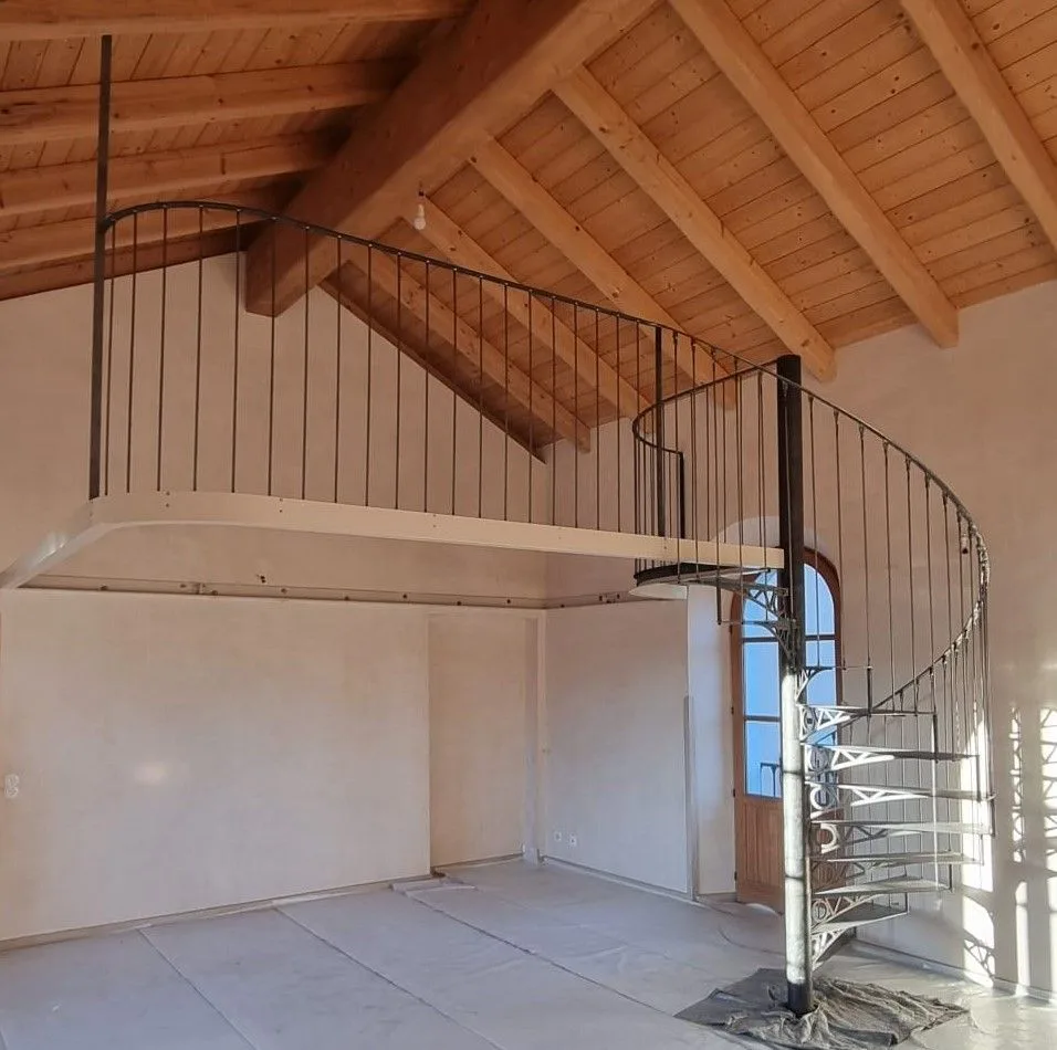 Soppalco sotto un tetto in legno con scala a chiocciola e parapetto in ferro